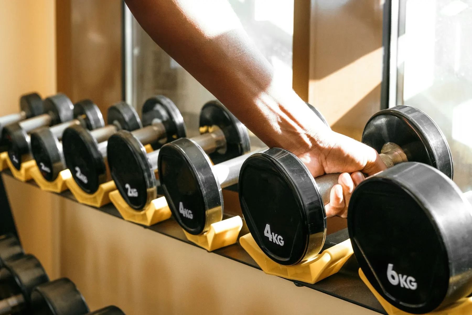A hand grabbing a dumbbell from a dumbbell rack in a gym