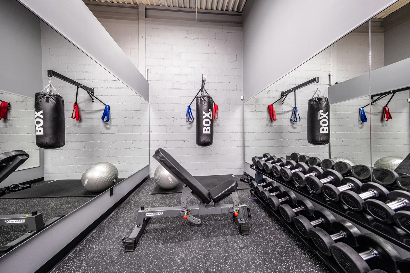 Zone de poids libres du gym corporatif Gicleurs F.F. avec banc, haltères et sacs de boxe.