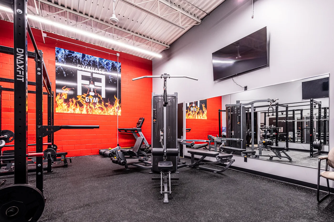 Salle d’entraînement Gicleurs F.F. avec mur rouge, appareil Matrix et rack DNAxFIT.